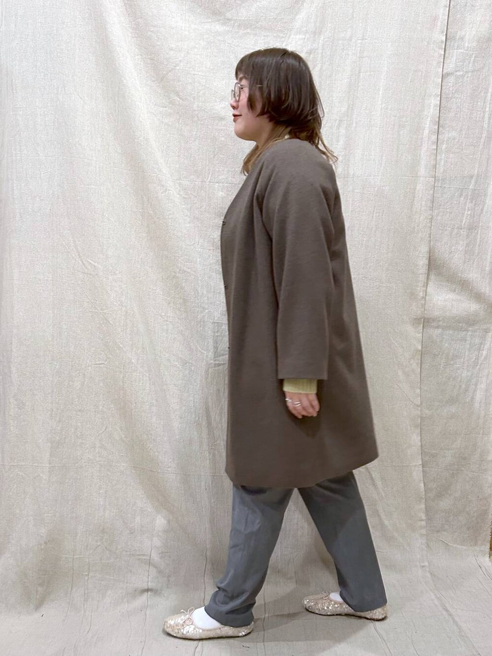 ブラウン系のノーカラーコート、グリーン系のニット/セーター、その他のその他パンツを着用したレディースの冬コーディネートの4枚目の写真