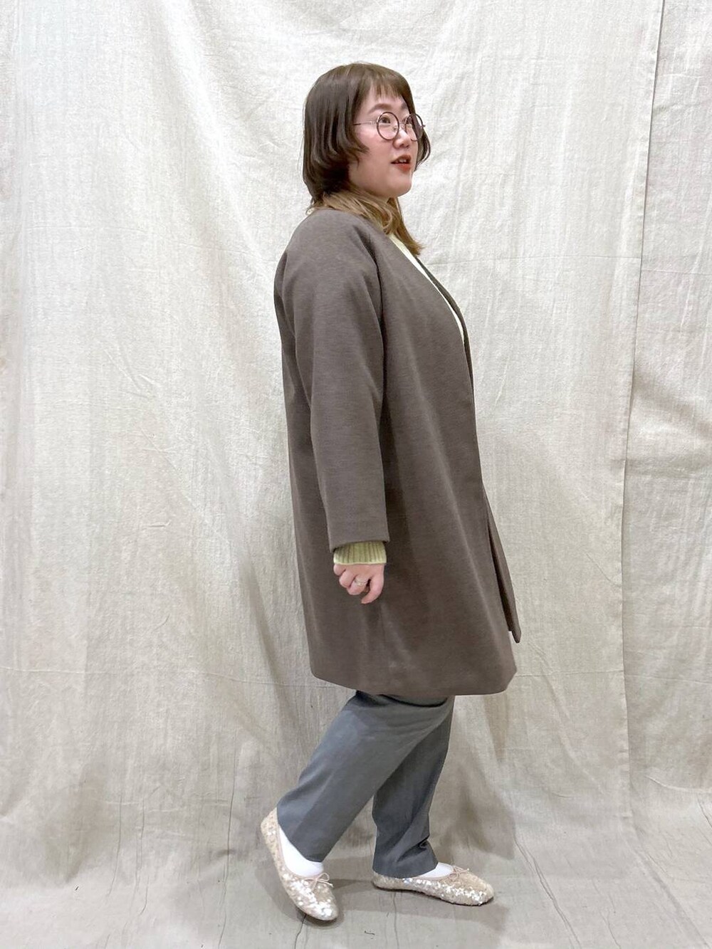 ブラウン系のノーカラーコート、グリーン系のニット/セーター、その他のその他パンツを着用したレディースの冬コーディネートの6枚目の写真