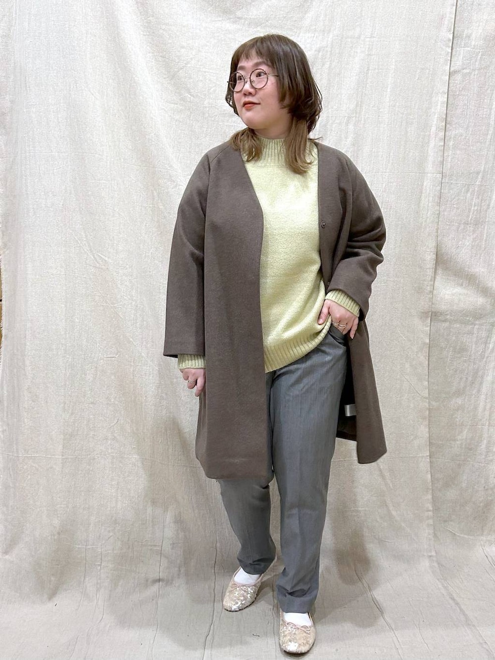 ブラウン系のノーカラーコート、グリーン系のニット/セーター、その他のその他パンツを着用したレディースの冬コーディネートの2枚目の写真