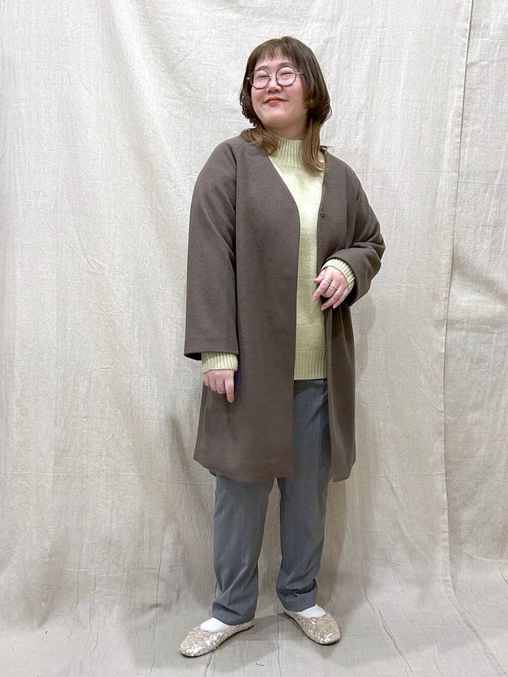 ブラウン系のノーカラーコート、グリーン系のニット/セーター、その他のその他パンツを着用したレディースの冬コーディネートの3枚目の写真