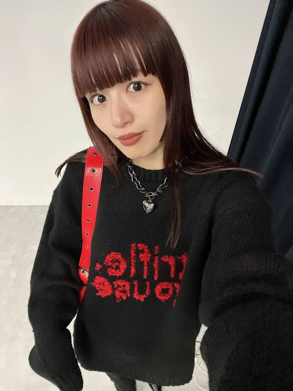 レッド系のショルダーバッグ、ブラック系のニット/セーター、ブラック系のネックレスを着用したレディースの秋コーディネートの5枚目の写真