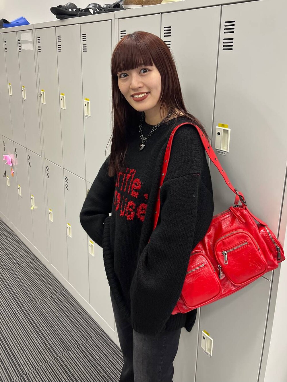 レッド系のショルダーバッグ、ブラック系のニット/セーター、ブラック系のネックレスを着用したレディースの秋コーディネートの2枚目の写真