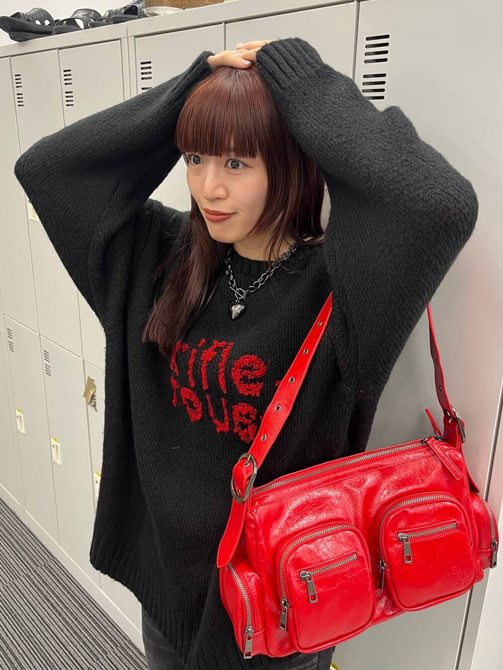 レッド系のショルダーバッグ、ブラック系のニット/セーター、ブラック系のネックレスを着用したレディースの秋コーディネートの3枚目の写真