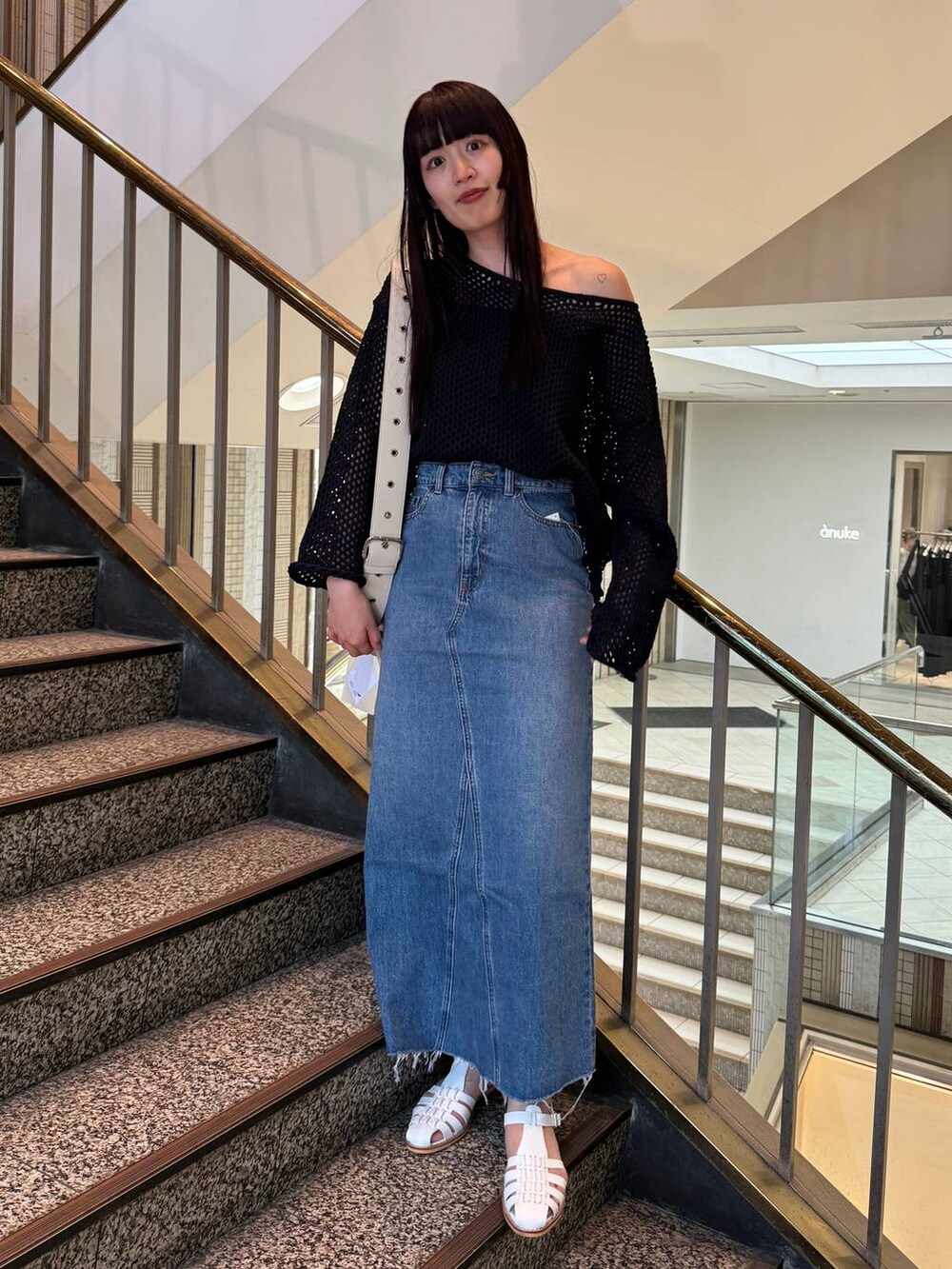 ブルー系のデニムスカート、ホワイト系のショルダーバッグ、ブルー系のニット/セーターを着用したレディースの春コーディネートの2枚目の写真