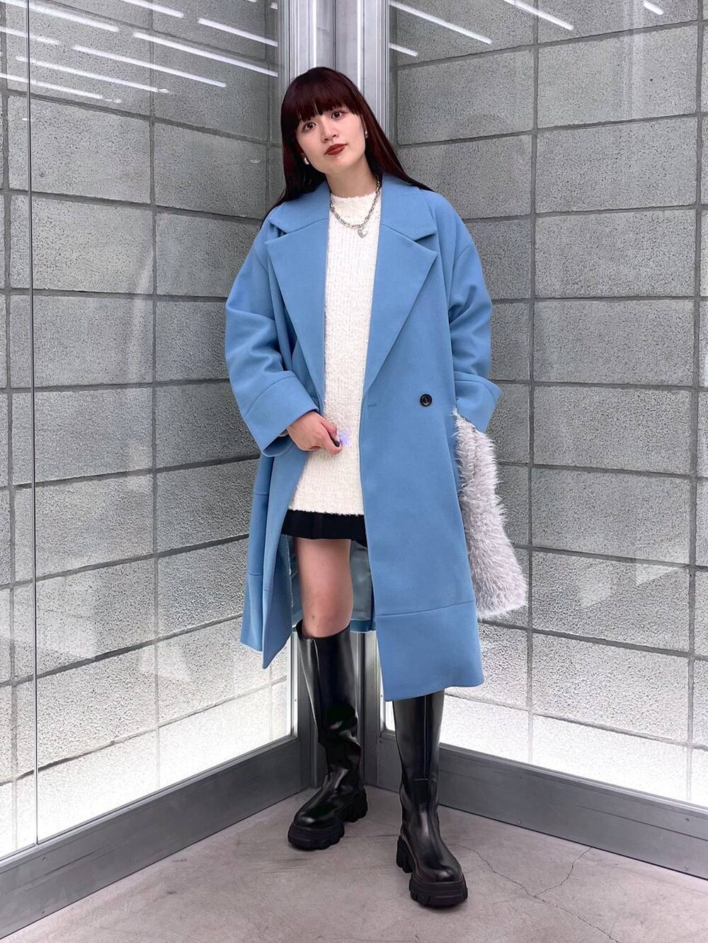 ブルー系のチェスターコート、ブラック系のブーツ、ホワイト系のハンドバッグを着用したレディースの秋コーディネートの5枚目の写真