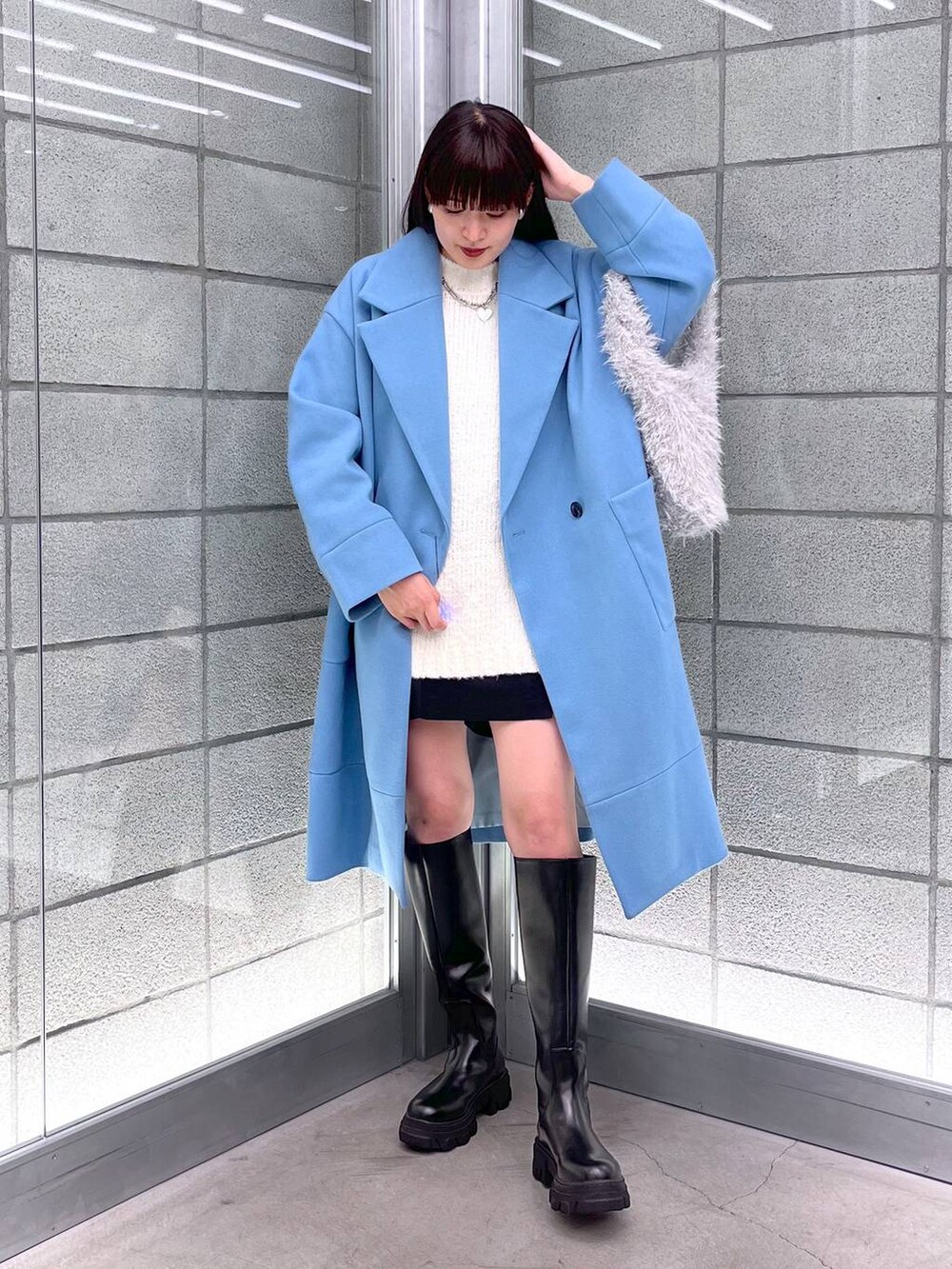 ブルー系のチェスターコート、ブラック系のブーツ、ホワイト系のハンドバッグを着用したレディースの秋コーディネートの2枚目の写真