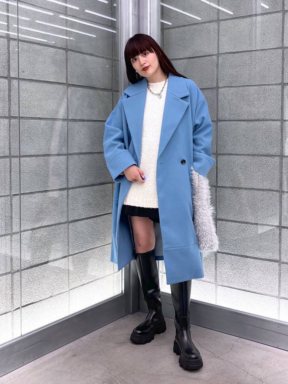 ブルー系のチェスターコート、ブラック系のブーツ、ホワイト系のハンドバッグを着用したレディースの秋コーディネートの4枚目の写真