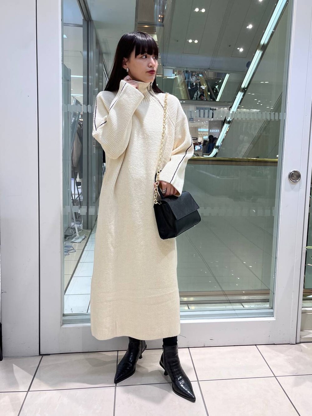 ブラック系のハンドバッグ、ブラック系のブーツ、ホワイト系のワンピースを着用したレディースの秋コーディネートの3枚目の写真