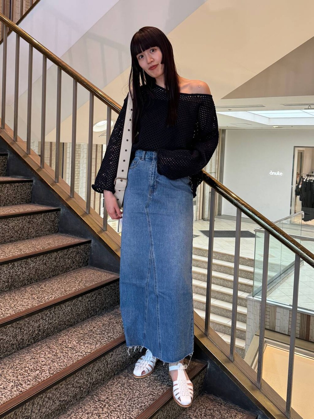 ブルー系のデニムスカート、ホワイト系のショルダーバッグ、ブルー系のニット/セーターを着用したレディースの春コーディネートの3枚目の写真