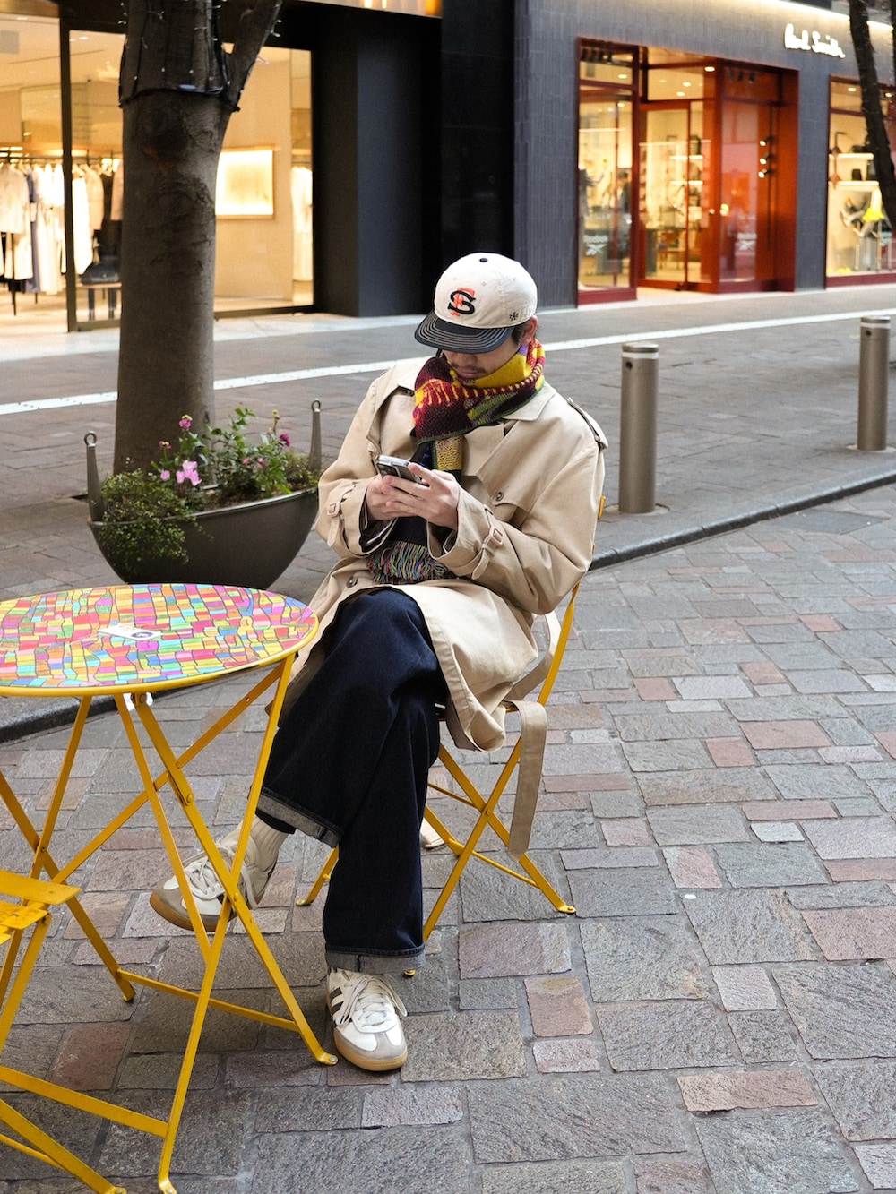 ホワイト系のスニーカー、ブルー系のデニムパンツ、ベージュ系のトレンチコートを着用したメンズの冬コーディネートの2枚目の写真