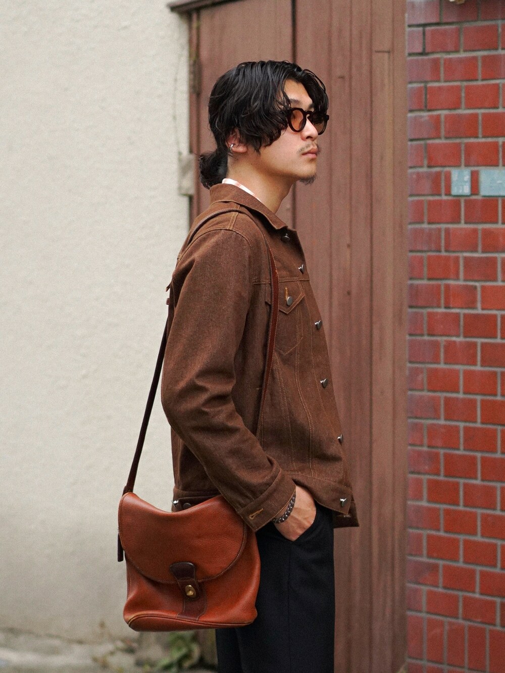 ブラック系のスラックス、ブラウン系のショルダーバッグ、ブラウン系のデニムジャケットを着用したメンズの秋コーディネートの3枚目の写真