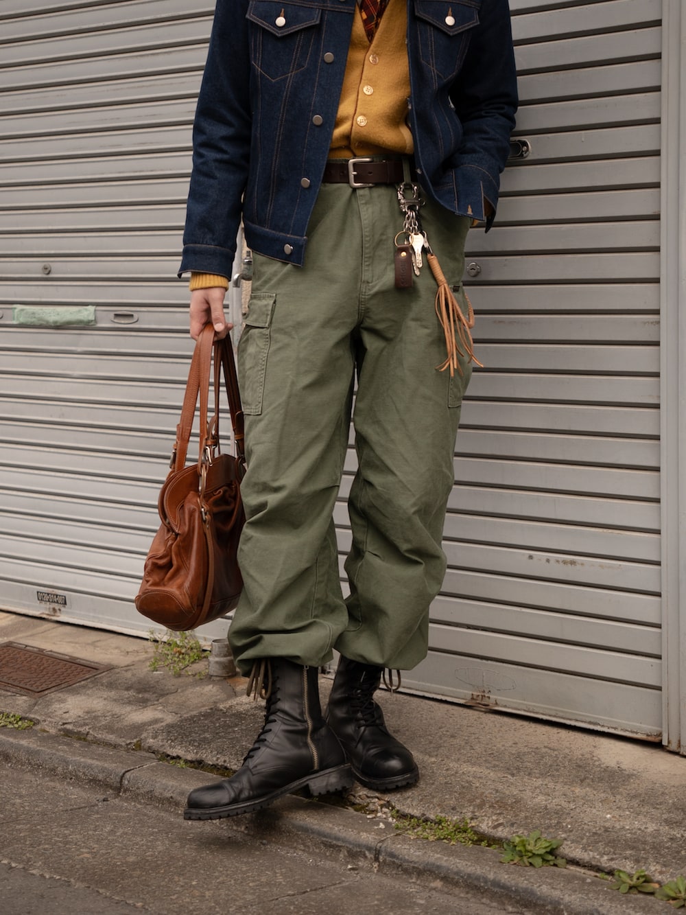 ブラウン系のボストンバッグ、ブラック系のブーツ、グリーン系のカーゴパンツを着用したメンズの春コーディネートの5枚目の写真