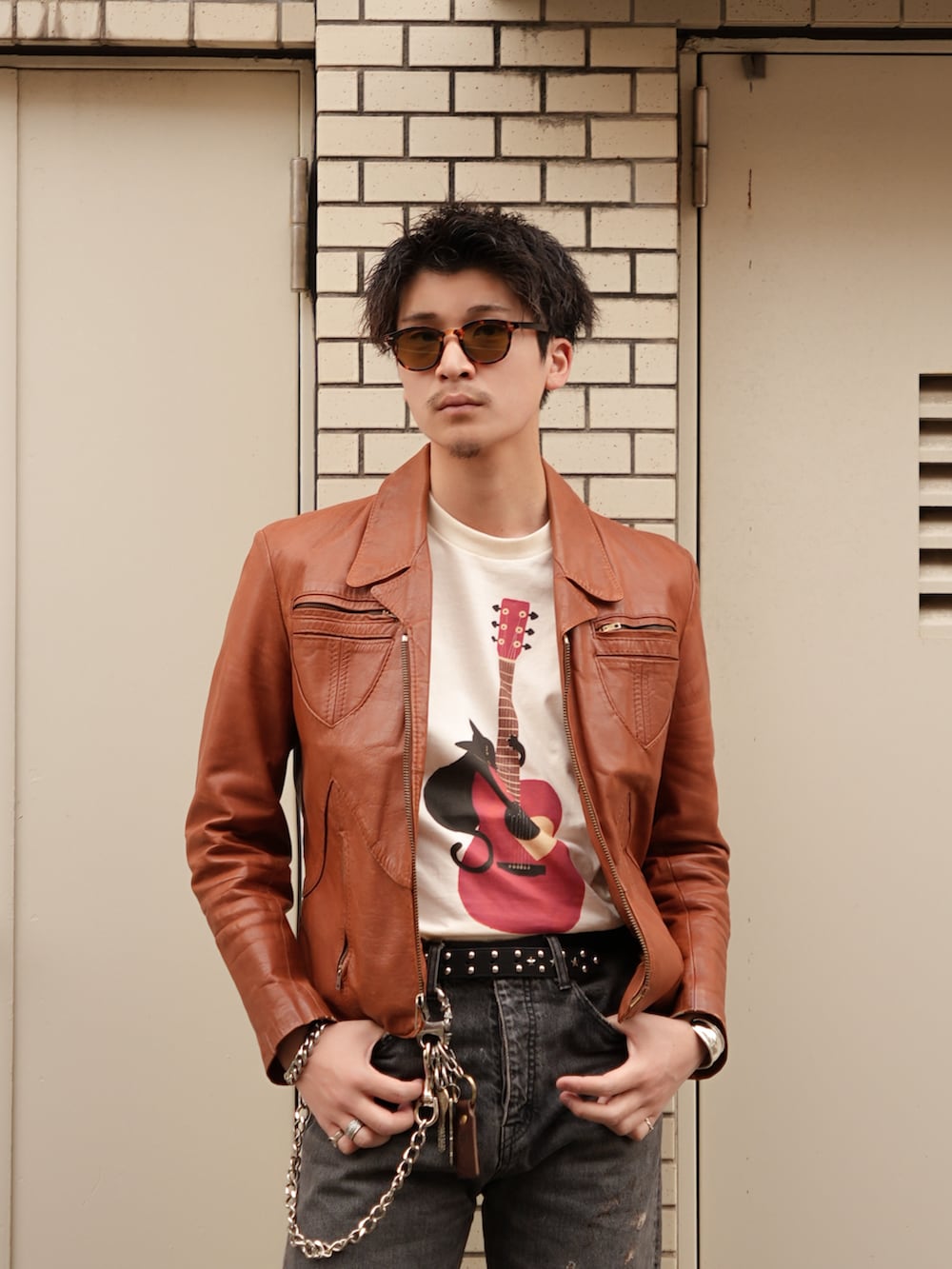 ブラック系のデニムパンツ、ベージュ系のTシャツ/カットソー、オレンジ系のジャケット/アウターを着用したメンズの春コーディネートの2枚目の写真