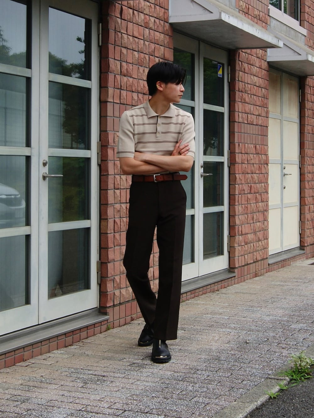 ブラウン系のスラックス、ベージュ系のポロシャツ、ブラック系のブーツを着用したメンズの夏コーディネートの2枚目の写真