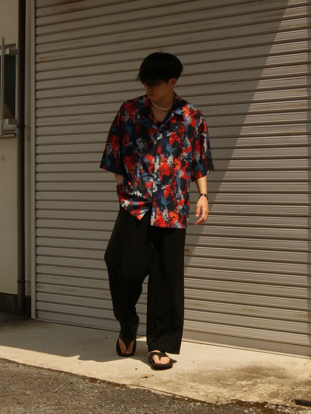 レッド系のトップス、ブラック系のスラックス、ブラック系のサンダルを着用したメンズの春コーディネートの2枚目の写真