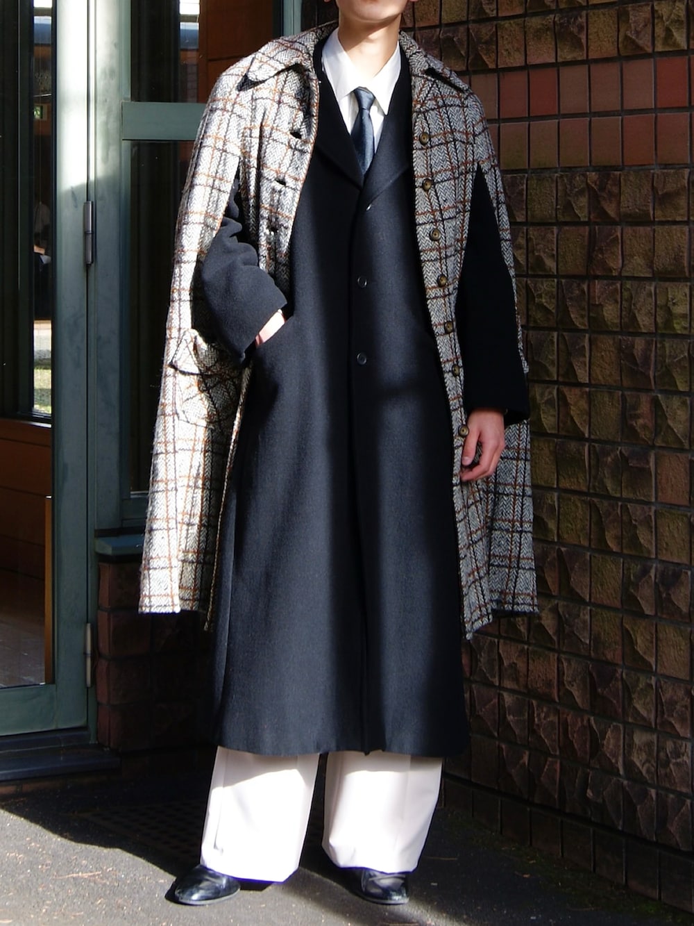 ブラック系のチェスターコート、シルバー系のポンチョ、ベージュ系のスラックスを着用したメンズの冬コーディネートの2枚目の写真