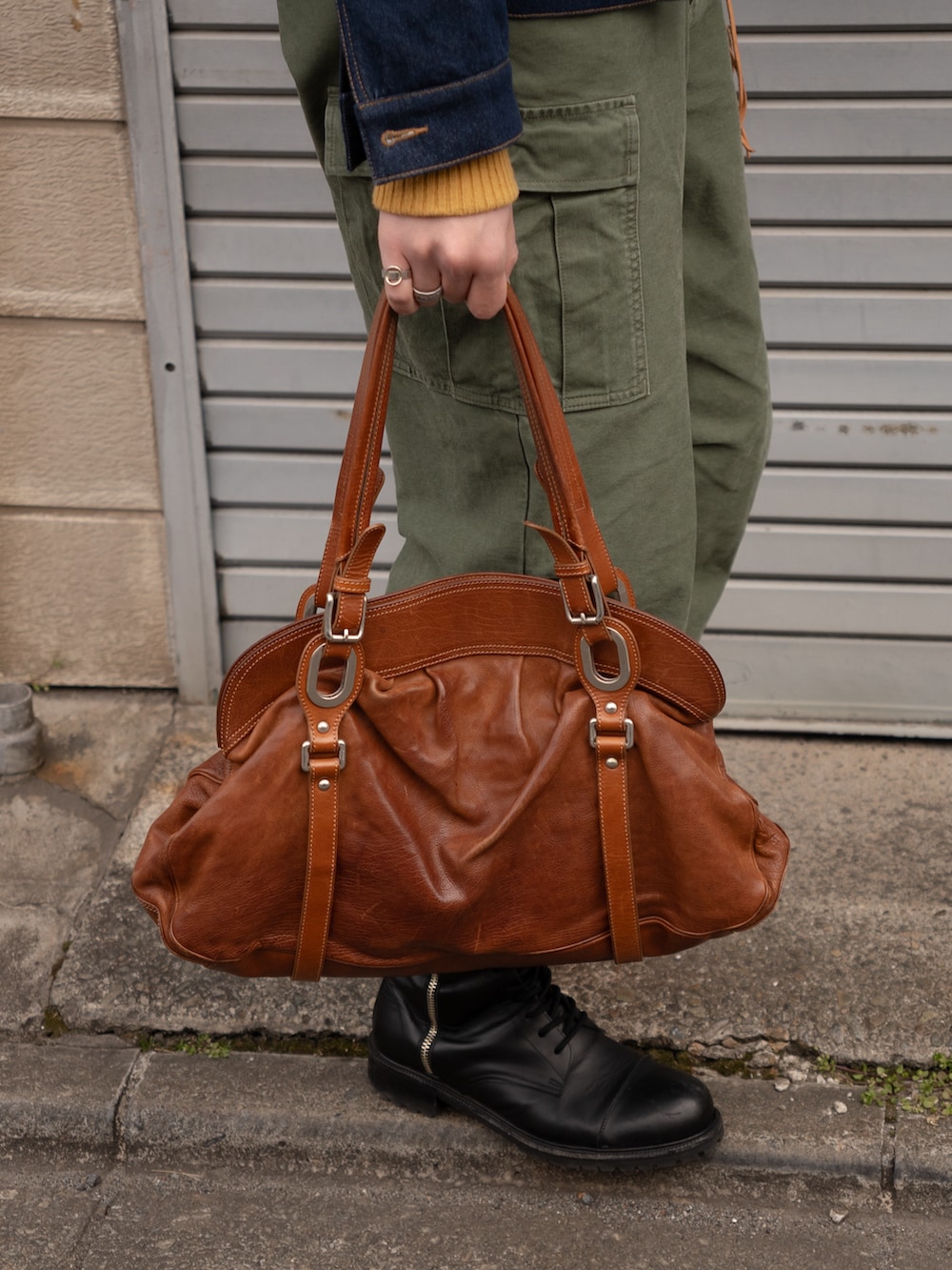 ブラウン系のボストンバッグ、ブラック系のブーツ、グリーン系のカーゴパンツを着用したメンズの春コーディネートの4枚目の写真