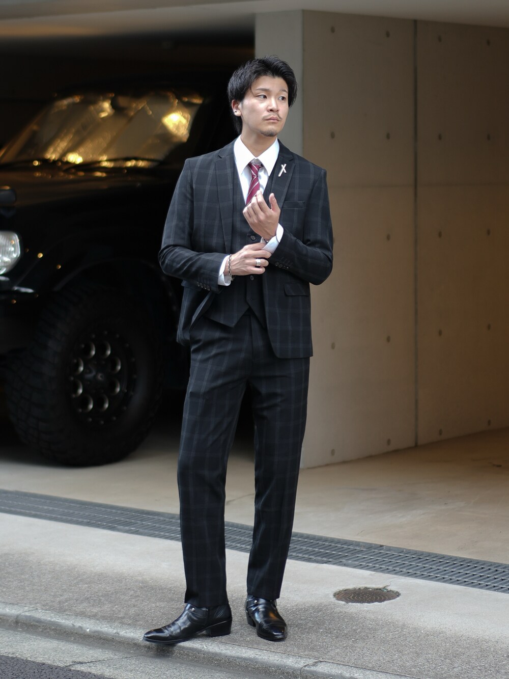 ブラック系のスーツセット、レッド系のネクタイ、ブラック系のブーツを着用したメンズの秋コーディネートの3枚目の写真