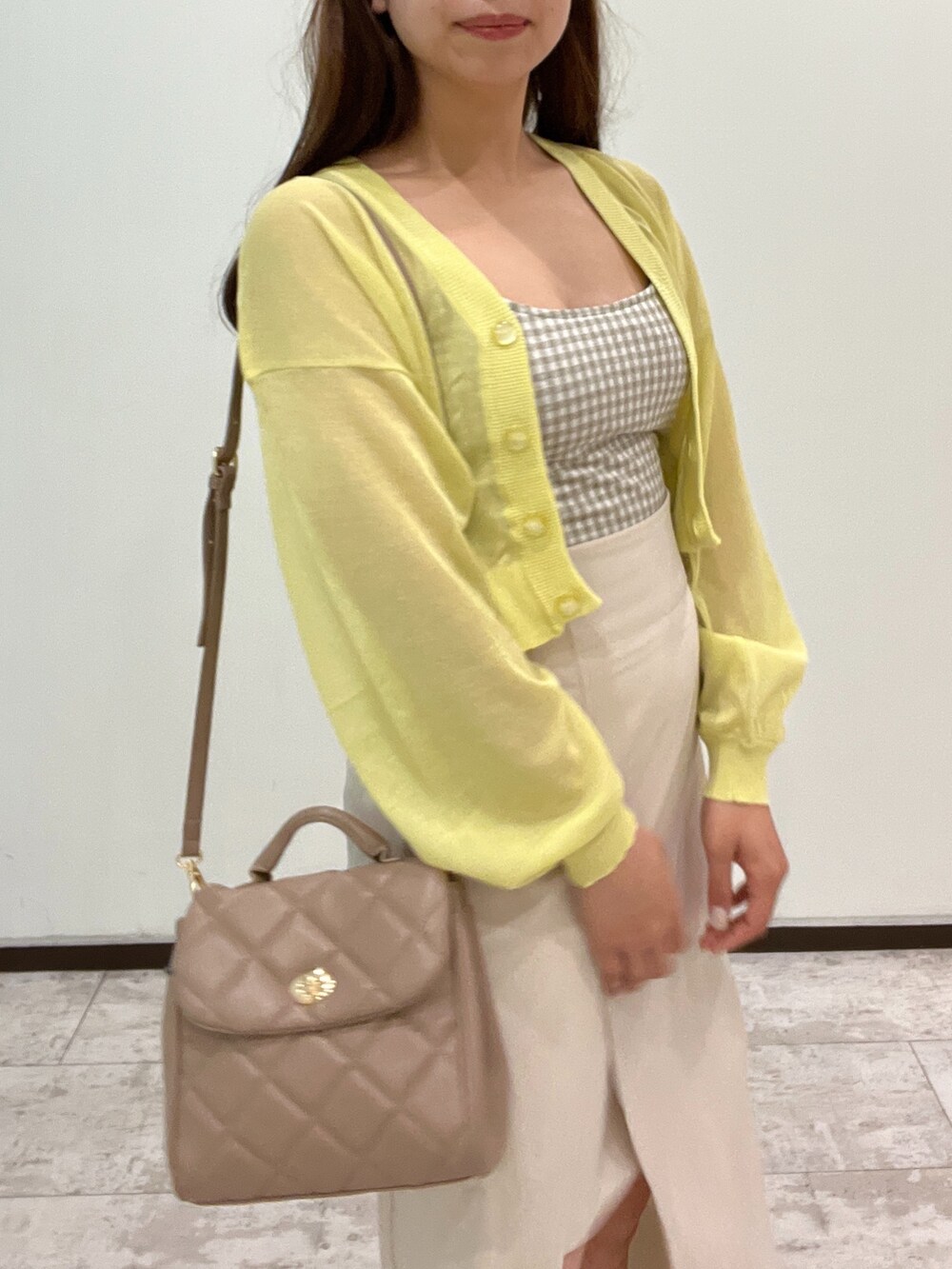 イエロー系のカーディガン/ボレロ、ベージュ系のキャミソール、ホワイト系のスカートを着用したレディースの春コーディネートの2枚目の写真