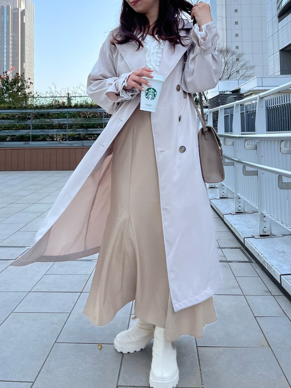 ベージュ系のトレンチコート、ベージュ系のスカート、ホワイト系のシャツ/ブラウスを着用したレディースの春コーディネートの2枚目の写真