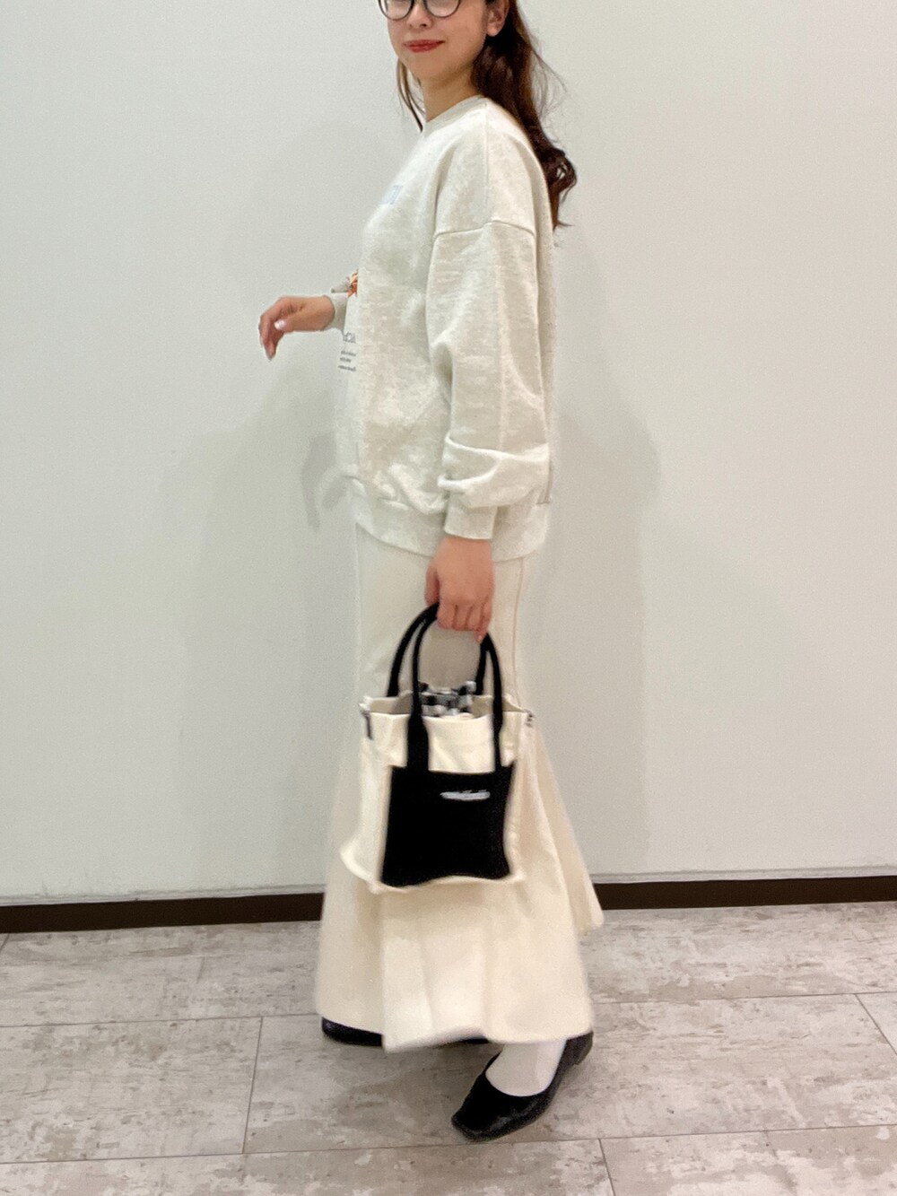グレー系のスウェット、ホワイト系のスカート、ブラック系のショルダーバッグを着用したレディースの春コーディネートの2枚目の写真