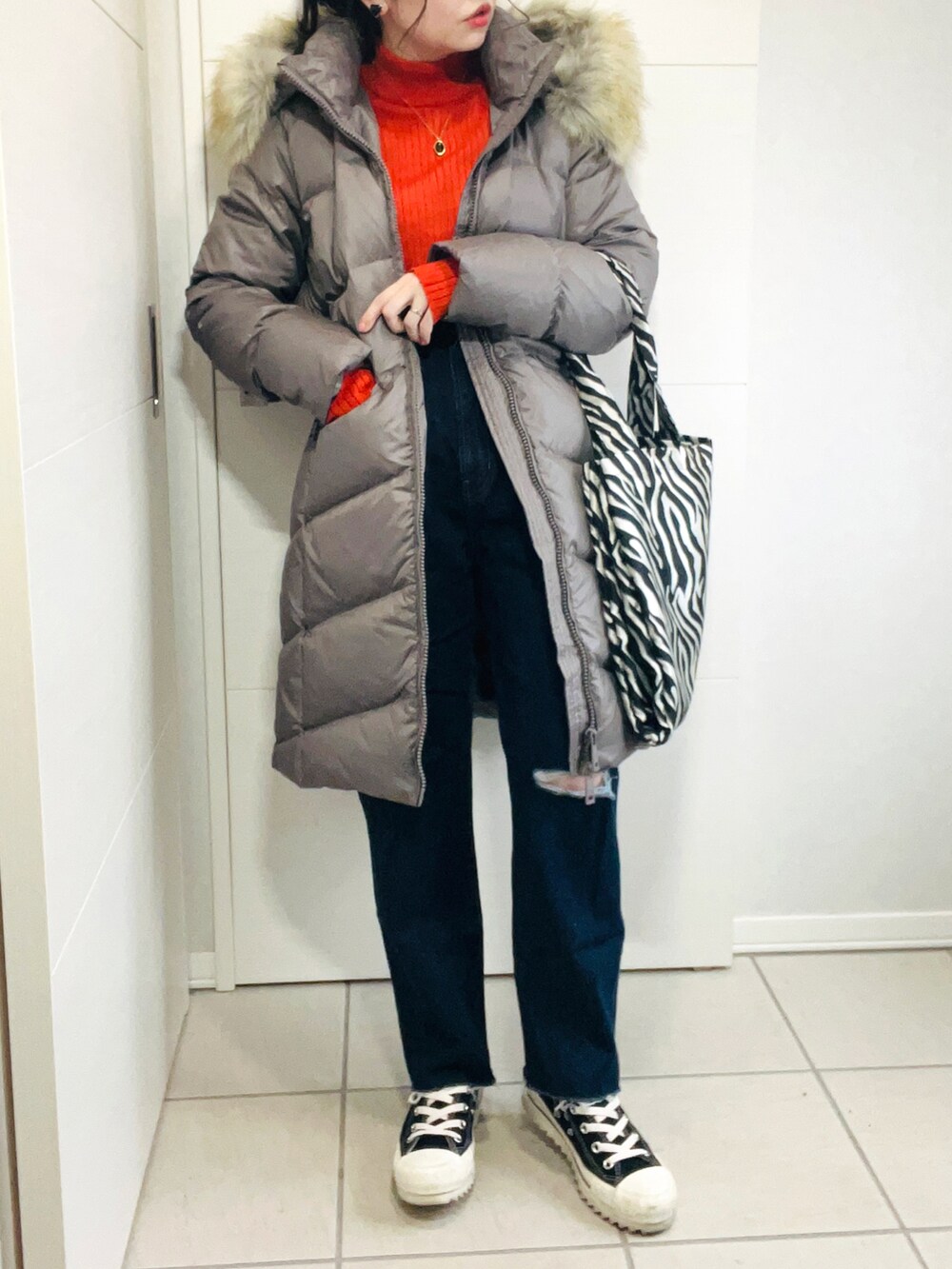 ブラウン系のダウンジャケット/コート、オレンジ系のニット/セーター、ブルー系のデニムパンツを着用したレディースの秋コーディネートの2枚目の写真