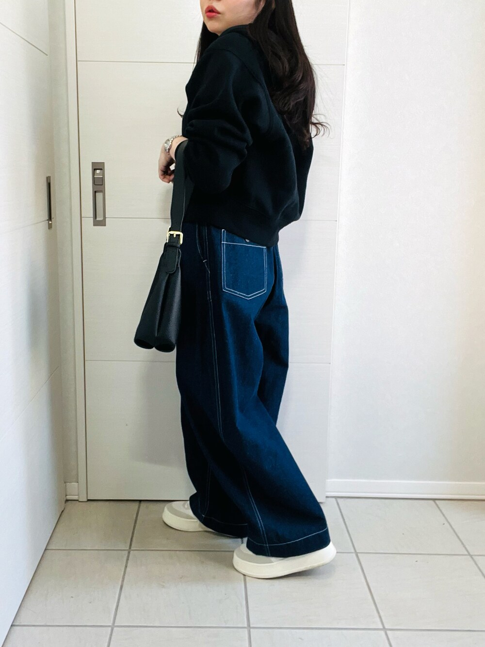 ブルー系のデニムパンツ、ホワイト系のスニーカー、ブラック系のショルダーバッグを着用したレディースの春コーディネートの5枚目の写真