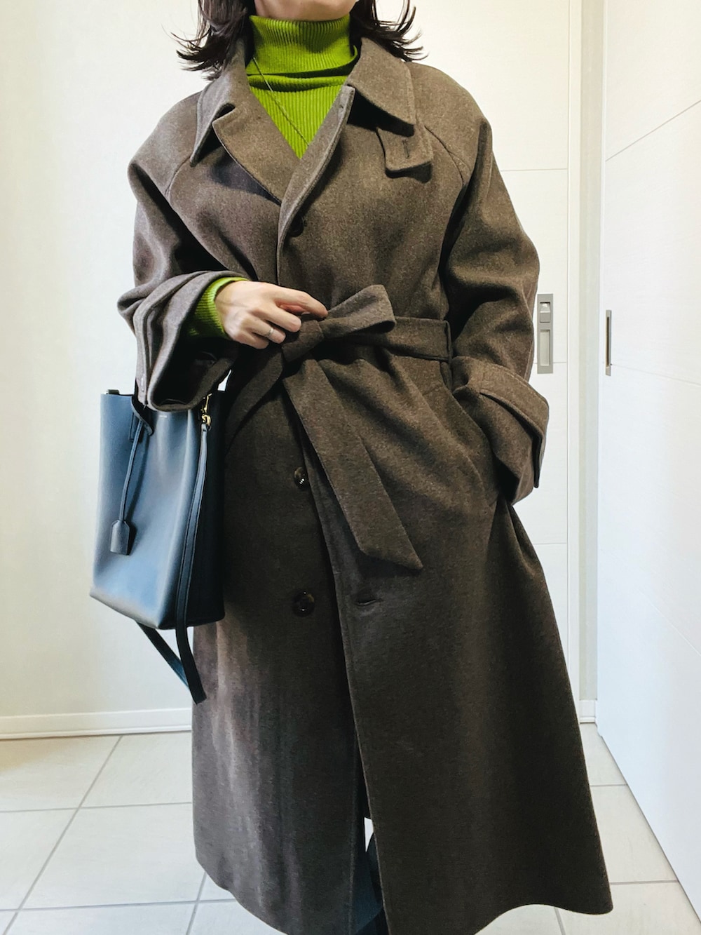 ブラウン系のステンカラーコート、グリーン系のニット/セーター、ブルー系のデニムパンツを着用したレディースの冬コーディネートの3枚目の写真