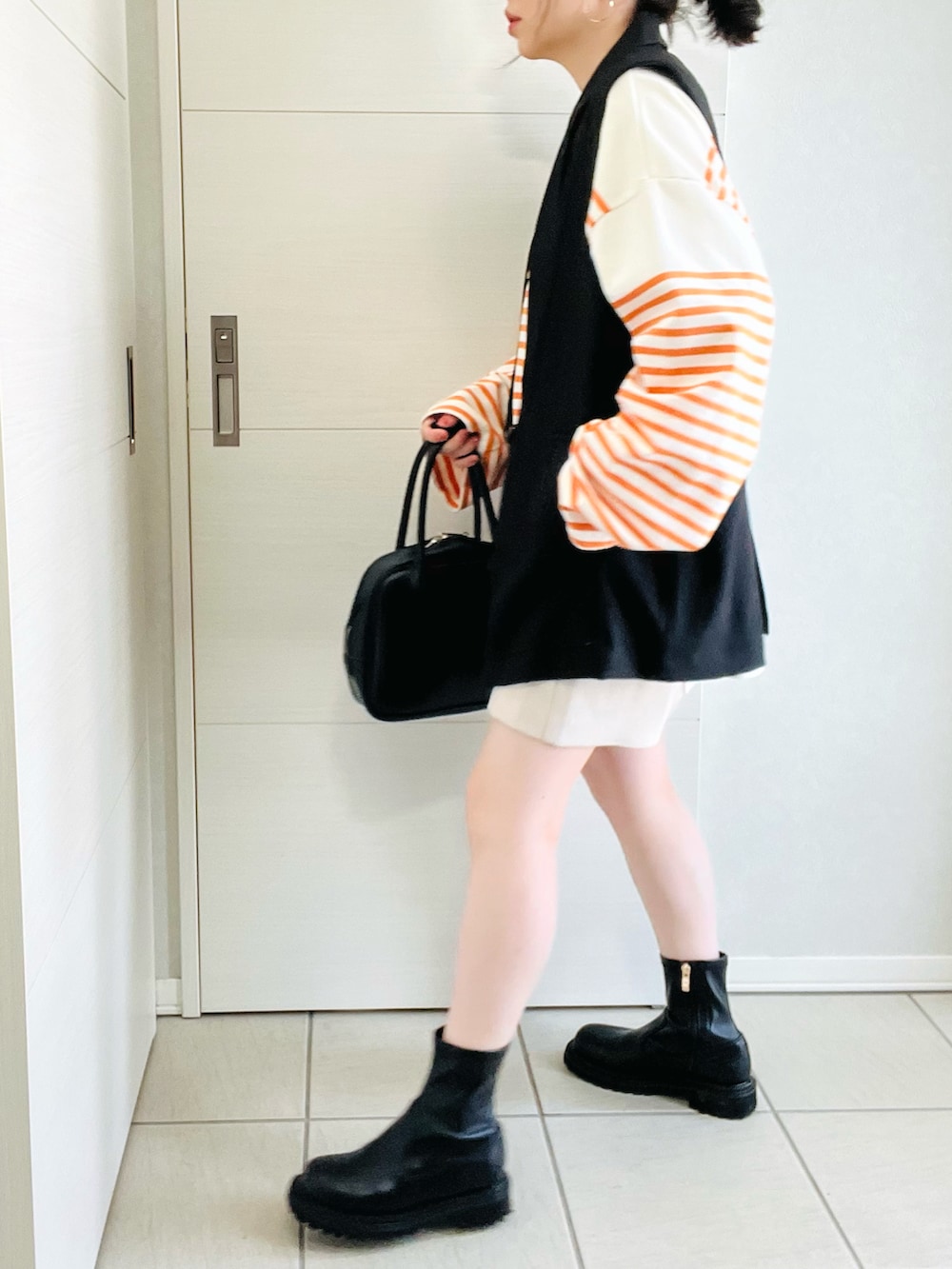 オレンジ系のTシャツ/カットソー、ブラック系のベスト、ホワイト系のスラックスを着用したレディースの春コーディネートの4枚目の写真