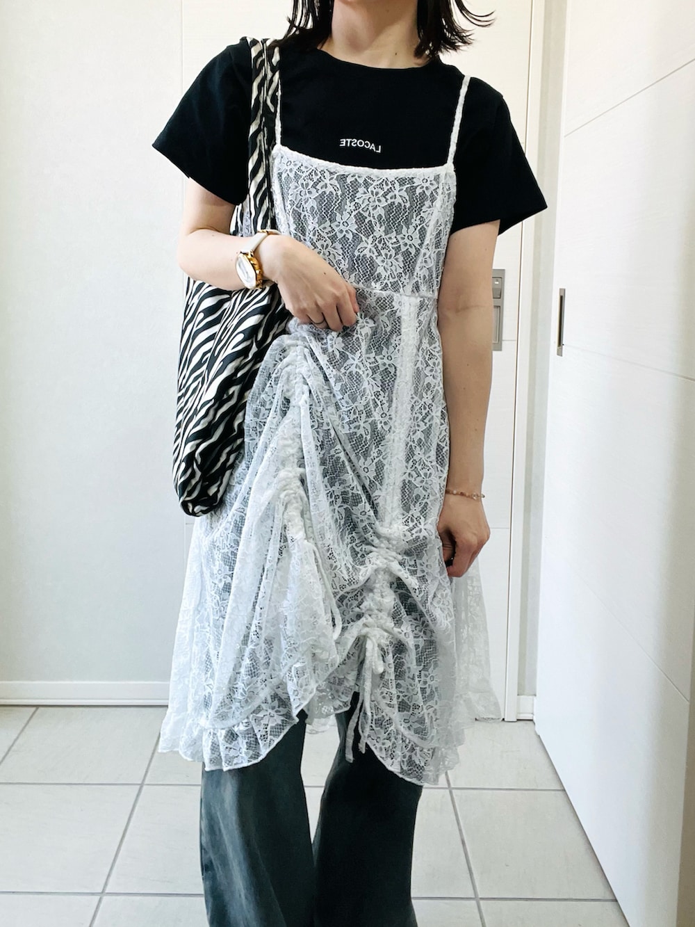 ホワイト系のチュニック、ブラック系のTシャツ/カットソー、ブルー系のデニムパンツを着用したレディースの春コーディネートの2枚目の写真