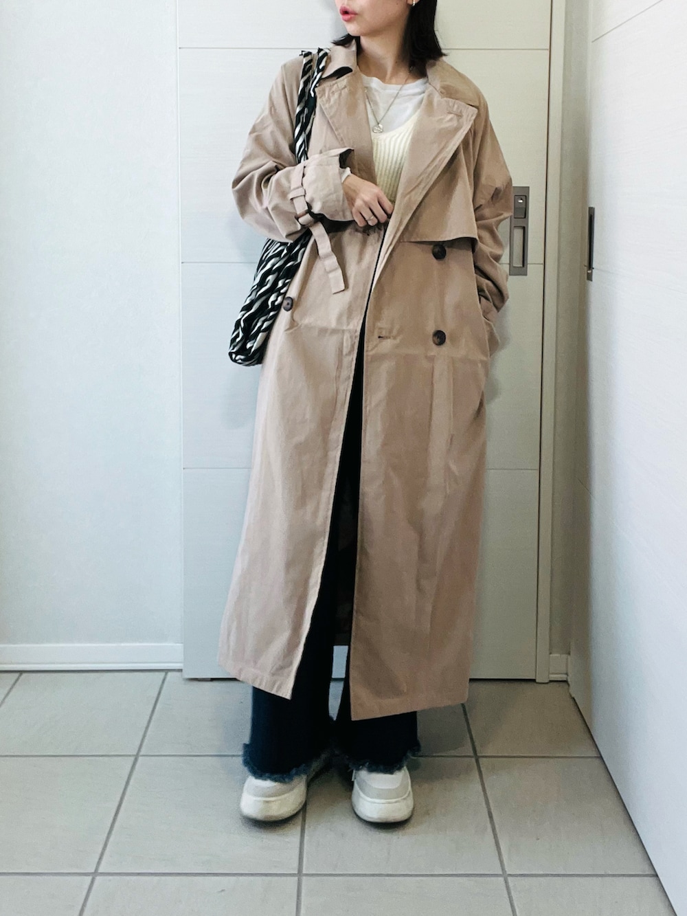 ベージュ系のトレンチコート、ホワイト系のニット/セーター、ブルー系のデニムパンツを着用したレディースの春コーディネートの5枚目の写真