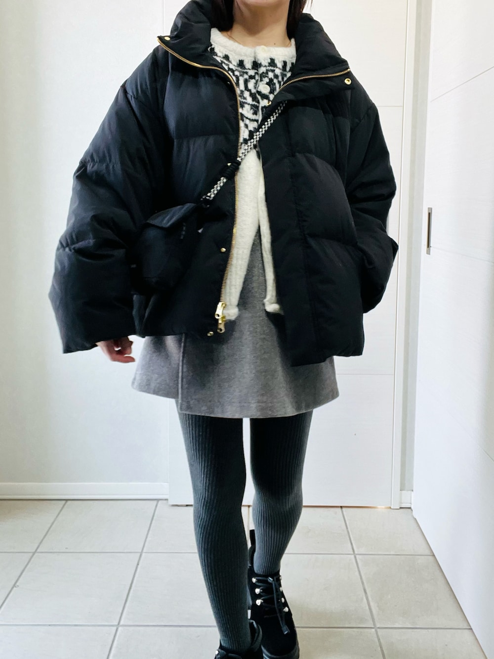 ブラック系のダウンジャケット/コート、ブラック系のブーツ、ホワイト系のカーディガン/ボレロを着用したレディースの春コーディネートの2枚目の写真