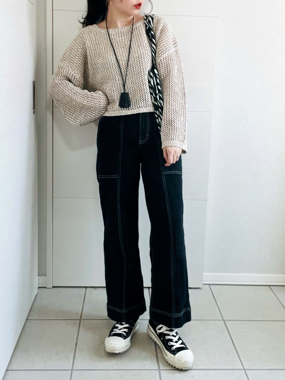 ベージュ系のニット/セーター、ブラック系のデニムパンツ、ブラック系のスニーカーを着用したレディースの春コーディネートの2枚目の写真
