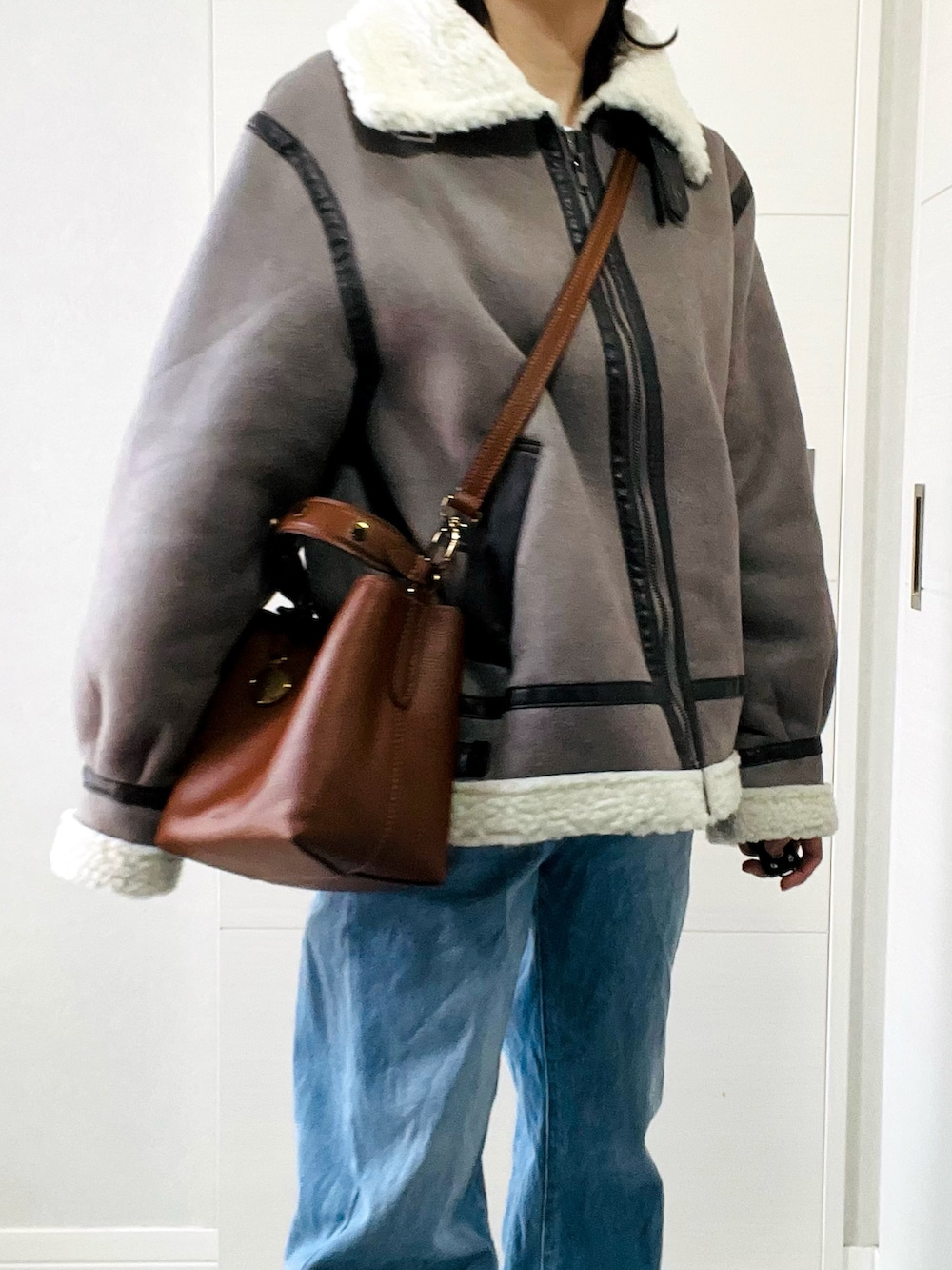 グレー系のムートンコート、ブルー系のデニムパンツ、ベージュ系のスリッポンを着用したレディースの冬コーディネートの2枚目の写真