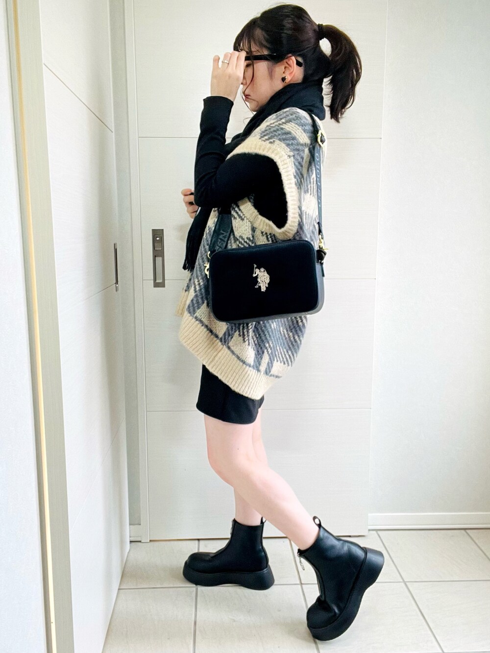 ブラック系のスカート、ホワイト系のベスト、ブラック系のブーツを着用したレディースの秋コーディネートの5枚目の写真