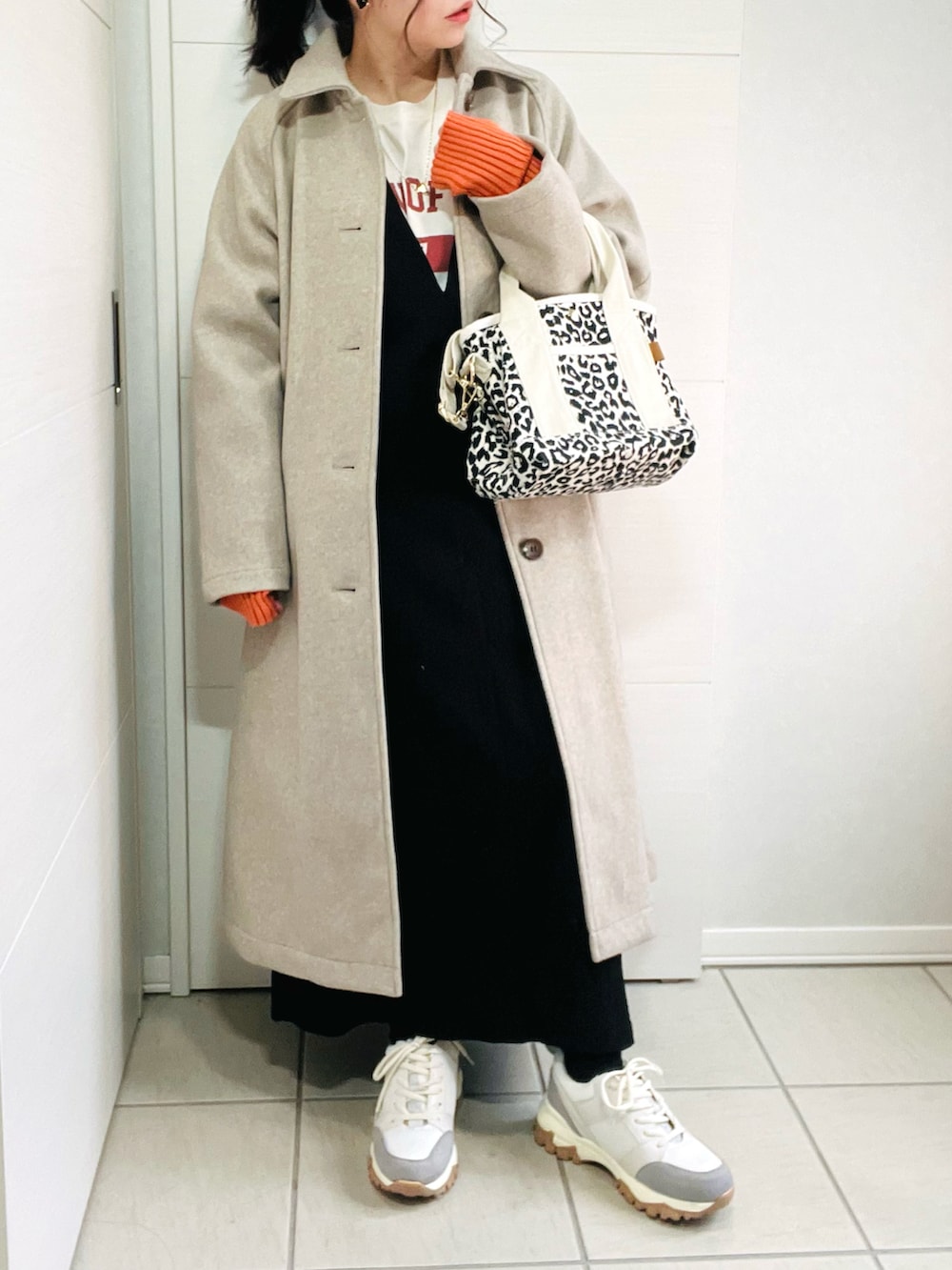 ベージュ系のステンカラーコート、ベージュ系のTシャツ/カットソー、ブラック系のワンピースを着用したレディースの秋コーディネートの2枚目の写真