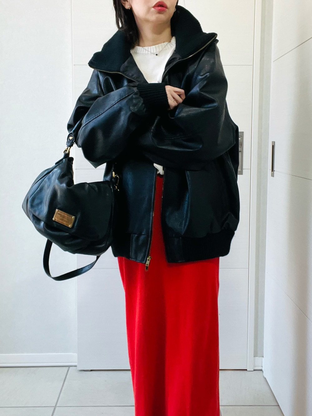 ブラック系のブルゾン、ホワイト系のニット/セーター、オレンジ系のスカートを着用したレディースの冬コーディネートの2枚目の写真