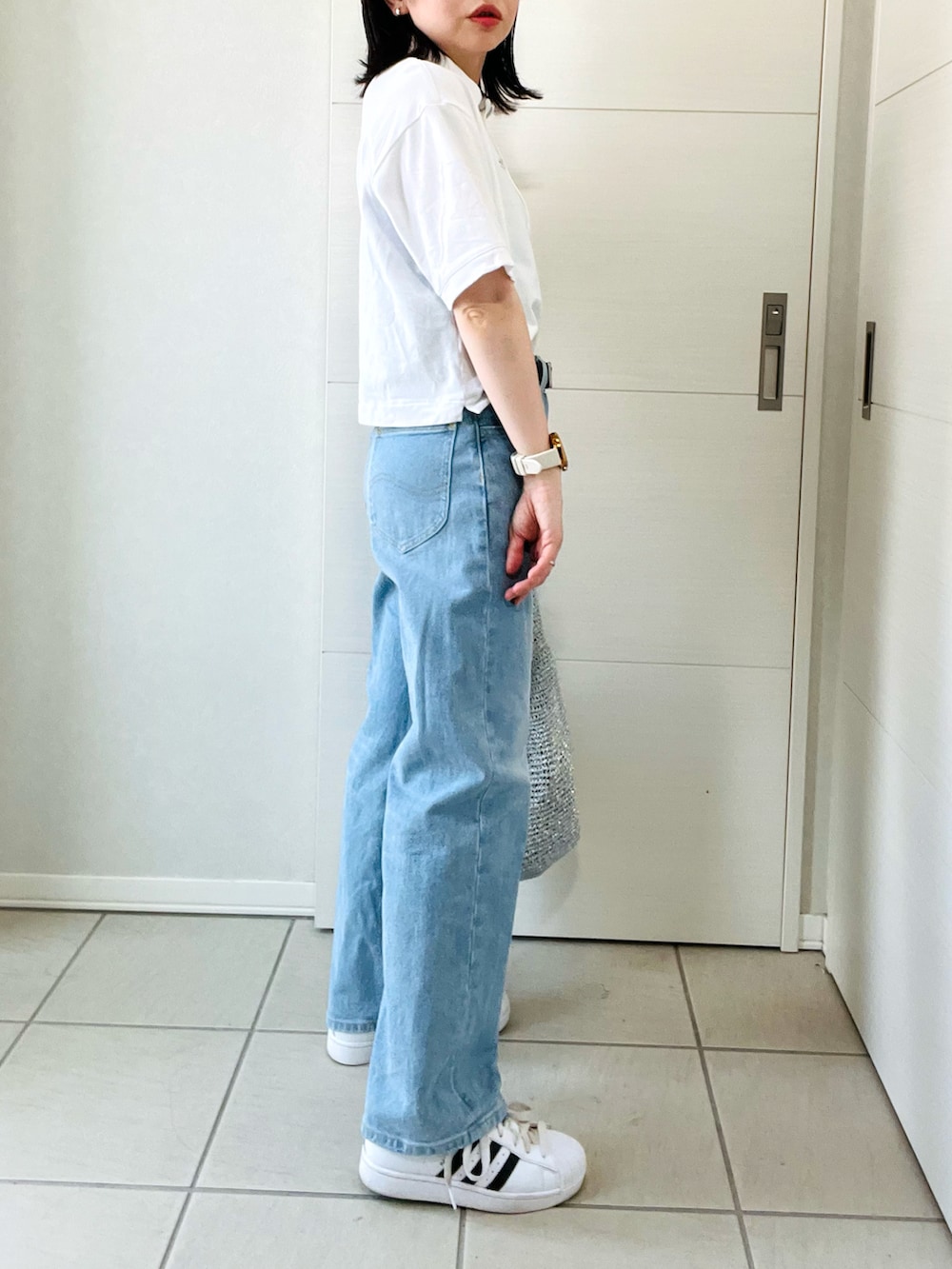 ホワイト系のポロシャツ、ブルー系のデニムパンツ、ホワイト系のスニーカーを着用したレディースの夏コーディネートの5枚目の写真