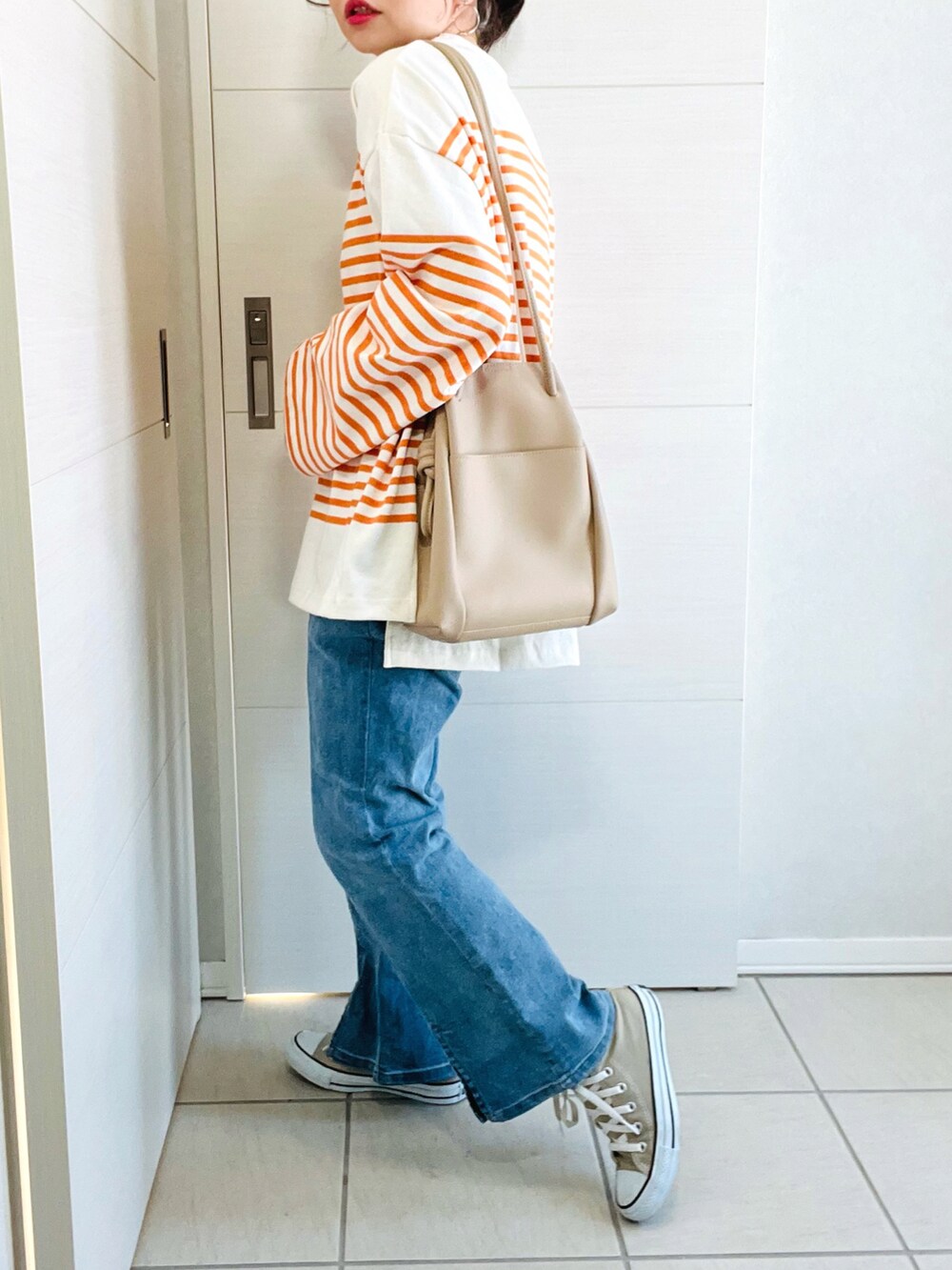 オレンジ系のTシャツ/カットソー、ブルー系のデニムパンツ、ベージュ系のトートバッグを着用したレディースの冬コーディネートの2枚目の写真