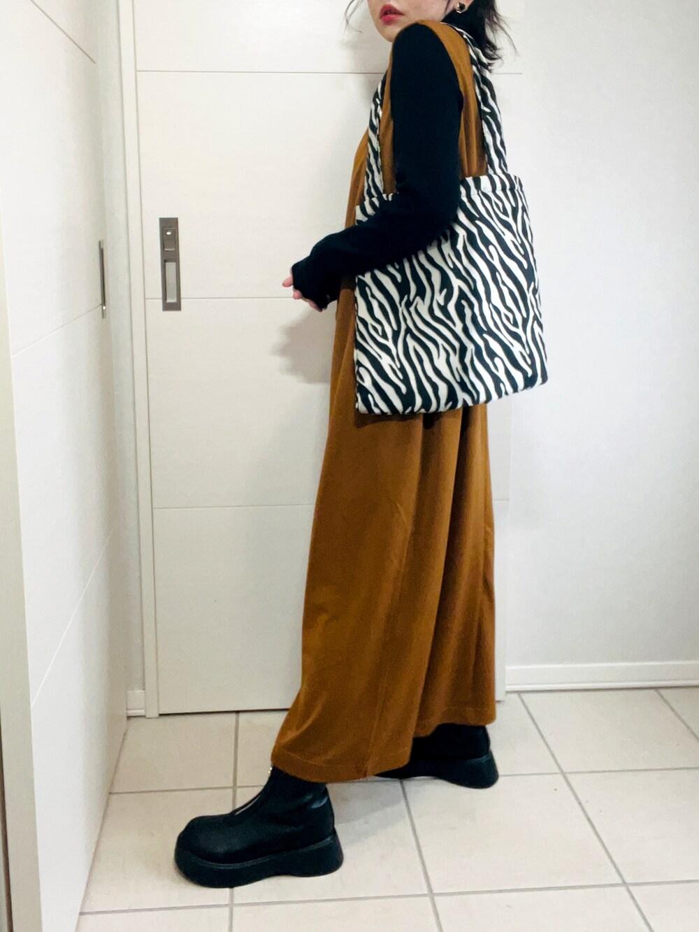 ブラウン系のサロペット/オーバーオール、ブラック系のニット/セーター、ブラック系のブーツを着用したレディースの秋コーディネートの4枚目の写真