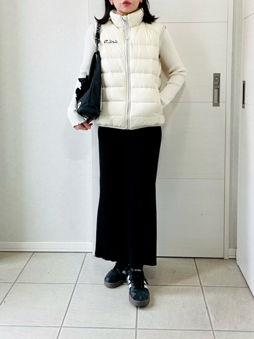 ホワイト系のダウンベスト、ホワイト系のニット/セーター、ブラック系のスカートを着用したレディースの秋コーディネートの4枚目の写真