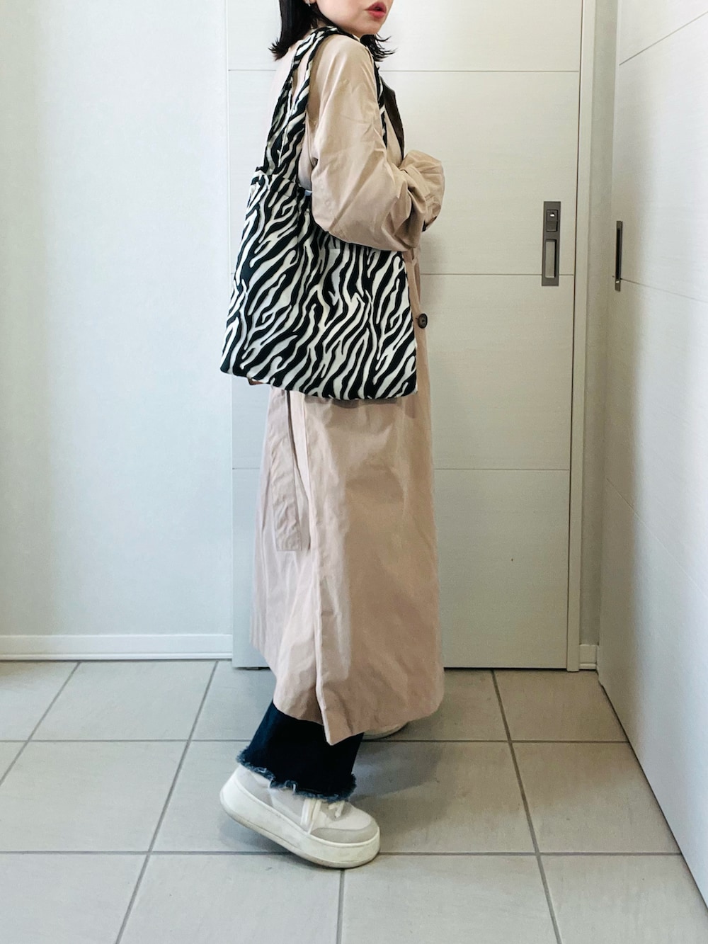 ベージュ系のトレンチコート、ホワイト系のニット/セーター、ブルー系のデニムパンツを着用したレディースの春コーディネートの4枚目の写真