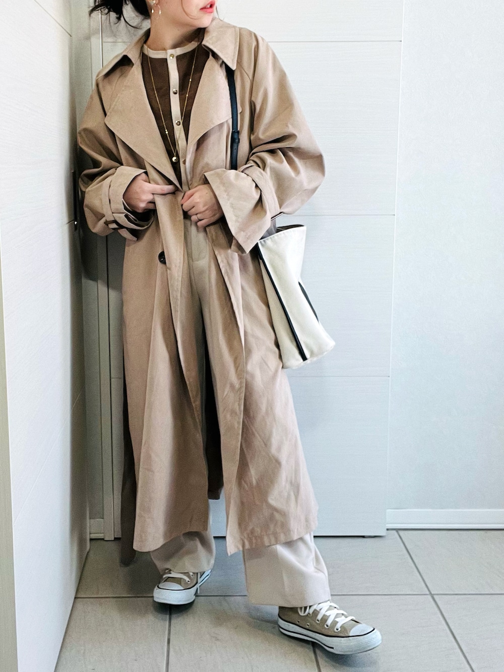 ベージュ系のトレンチコート、ブラウン系のTシャツ/カットソー、ホワイト系のスラックスを着用したレディースの冬コーディネートの3枚目の写真