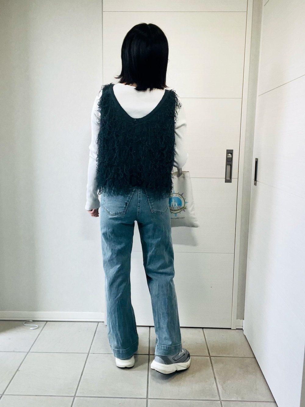 グレー系のベスト、グレー系のスニーカー、ブルー系のデニムパンツを着用したレディースの春コーディネートの3枚目の写真