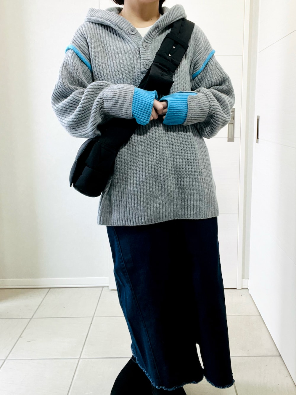 グレー系のニット/セーター、ブルー系のスカート、ブラック系のブーツを着用したレディースの冬コーディネートの2枚目の写真