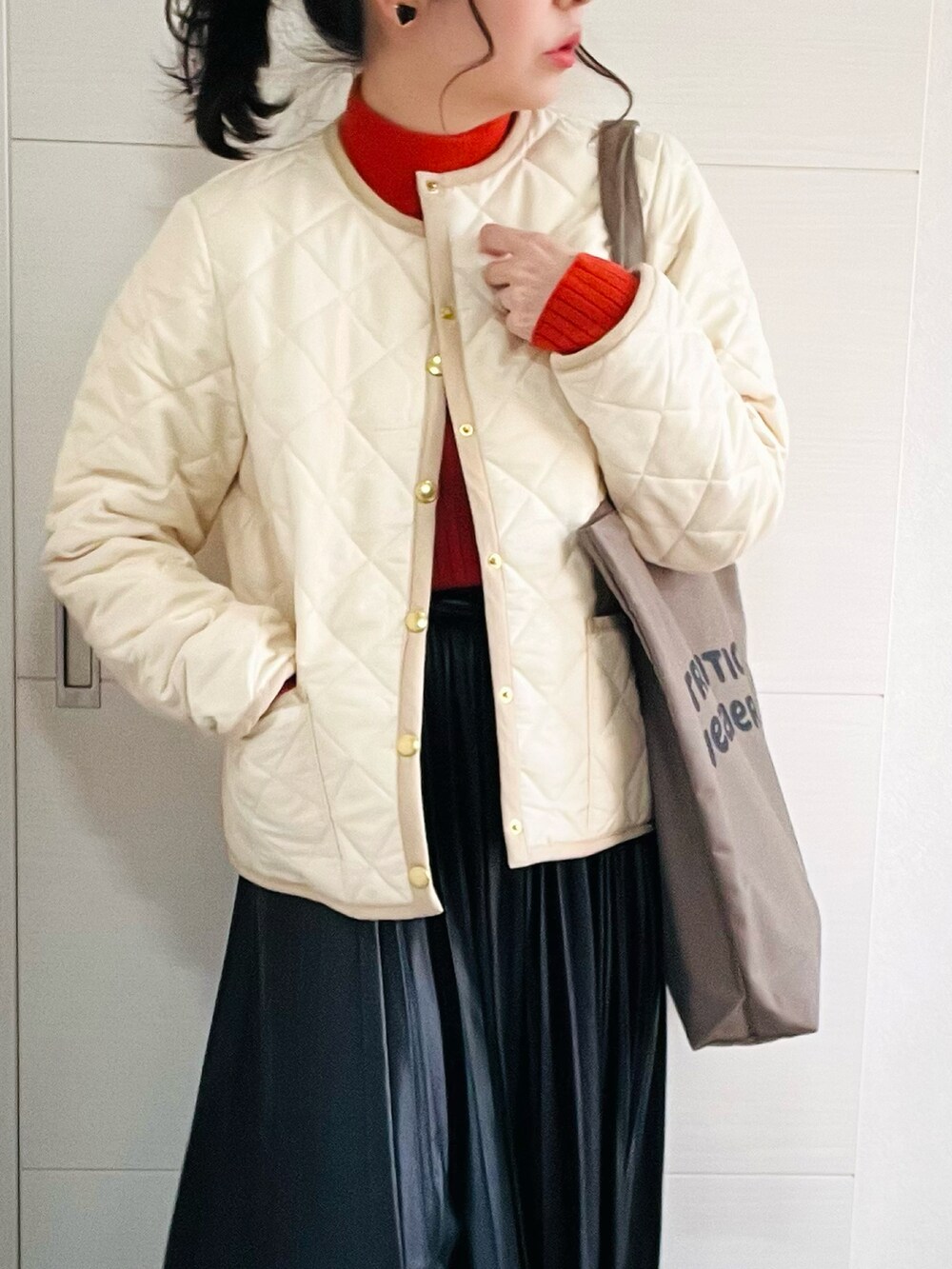 ホワイト系のノーカラージャケット、オレンジ系のニット/セーター、ブラック系のスカートを着用したレディースの秋コーディネートの2枚目の写真