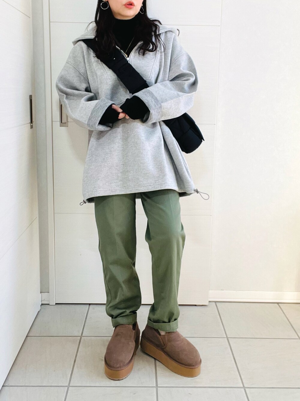 グレー系のパーカー、ブラック系のニット/セーター、グリーン系のチノパンツを着用したレディースの冬コーディネートの2枚目の写真