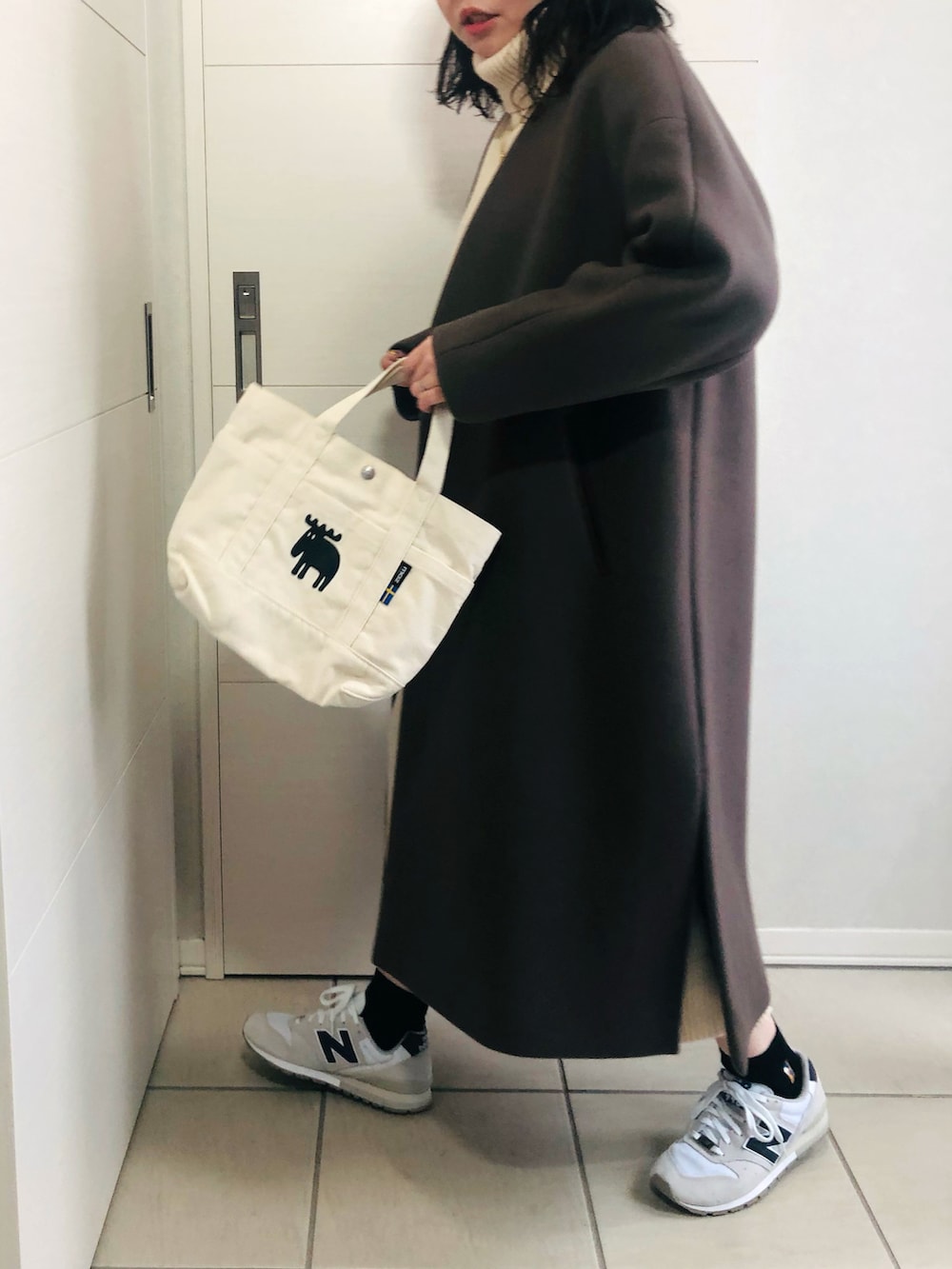 ブラウン系のノーカラーコート、ホワイト系のワンピース、ホワイト系のスニーカーを着用したレディースの秋コーディネートの5枚目の写真