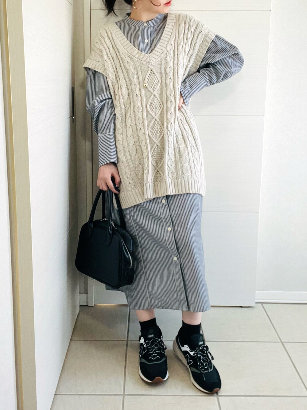 ブラック系のワンピース、ホワイト系のベスト、ブラック系のスニーカーを着用したレディースの春コーディネートの2枚目の写真