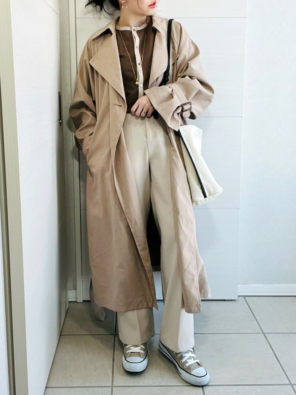 ベージュ系のトレンチコート、ブラウン系のTシャツ/カットソー、ホワイト系のスラックスを着用したレディースの冬コーディネートの2枚目の写真